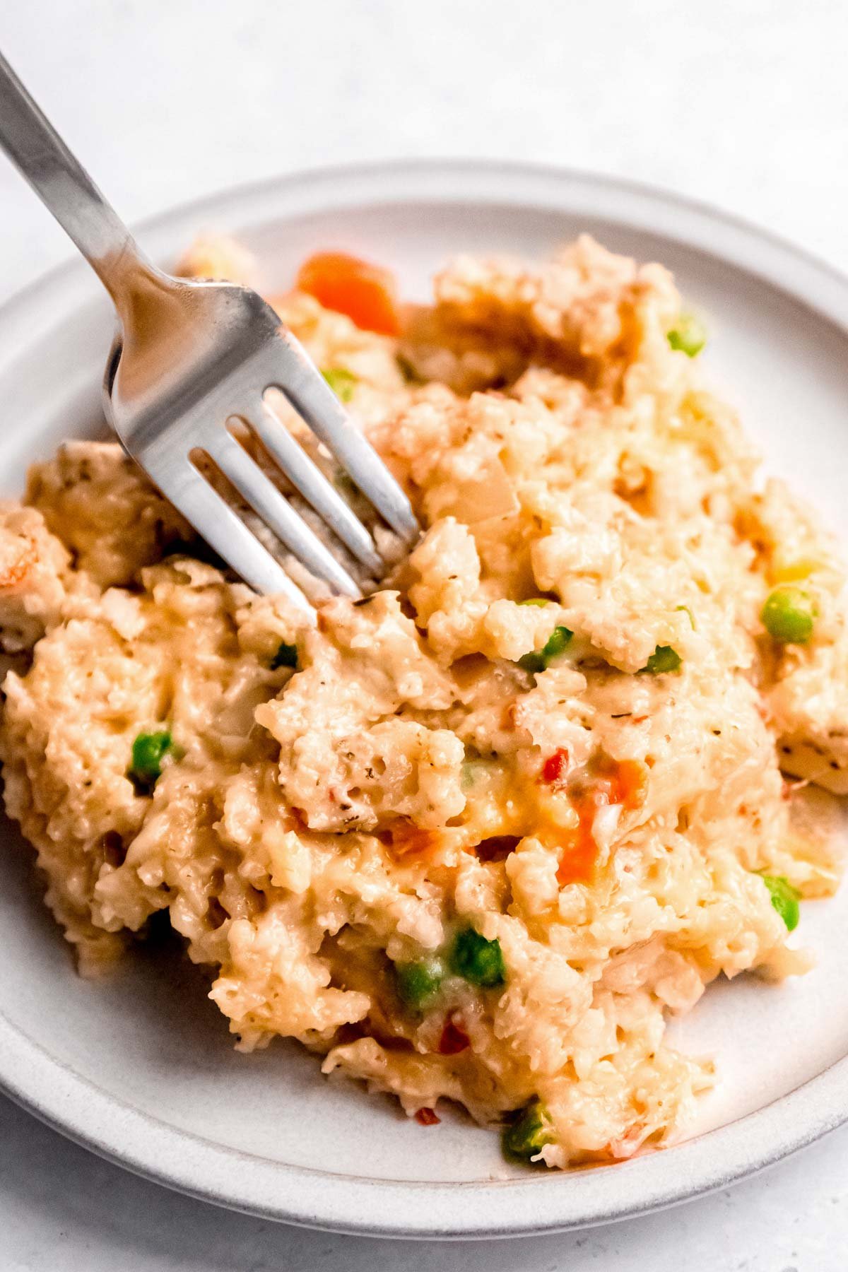 a fork in a big serving of chicken and rice with carrots and peas on a white plate