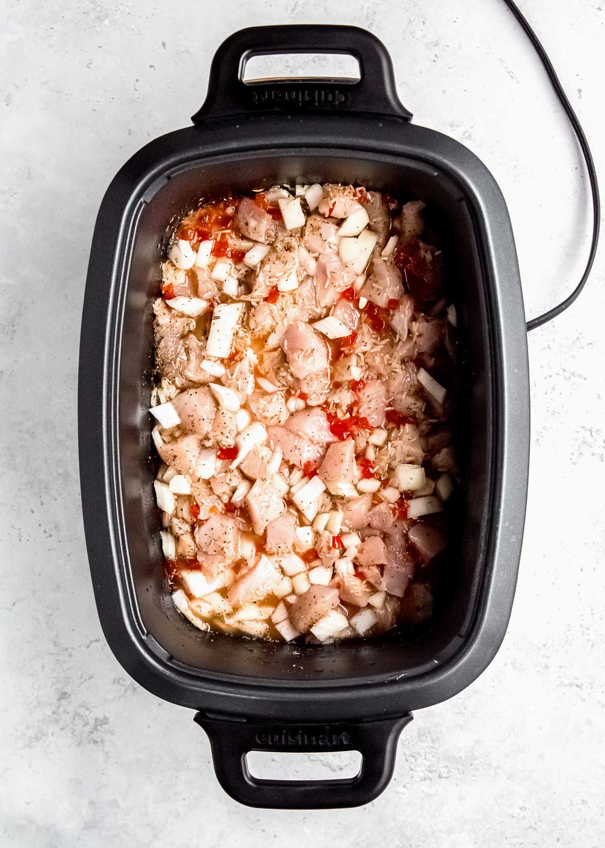 chicken and rice cooking in a crockpot with chopped onions, pimentos, and seasonings in chicken stock