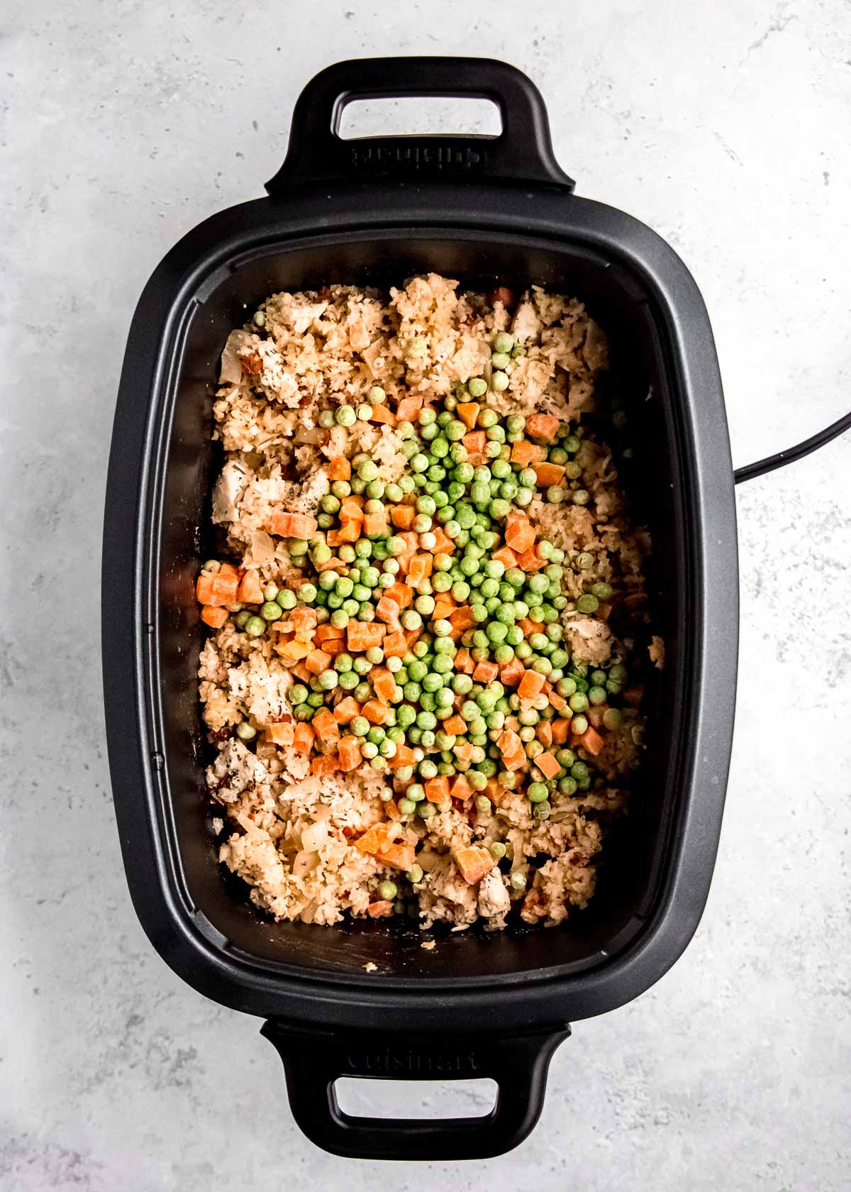 peas and carrots added to a crockpot full of chicken and rice