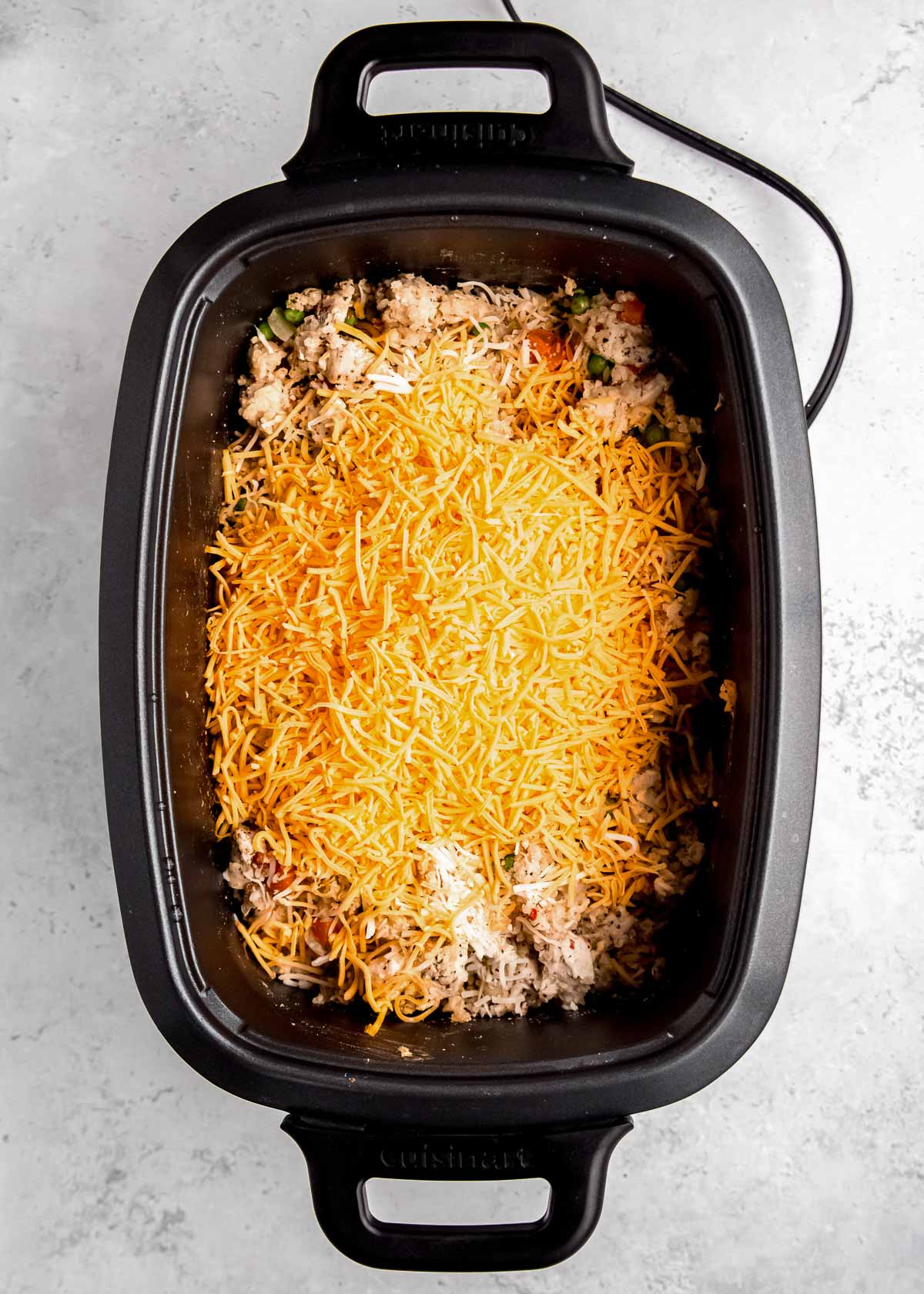 shredded cheese added to a crockpot full of chicken and rice