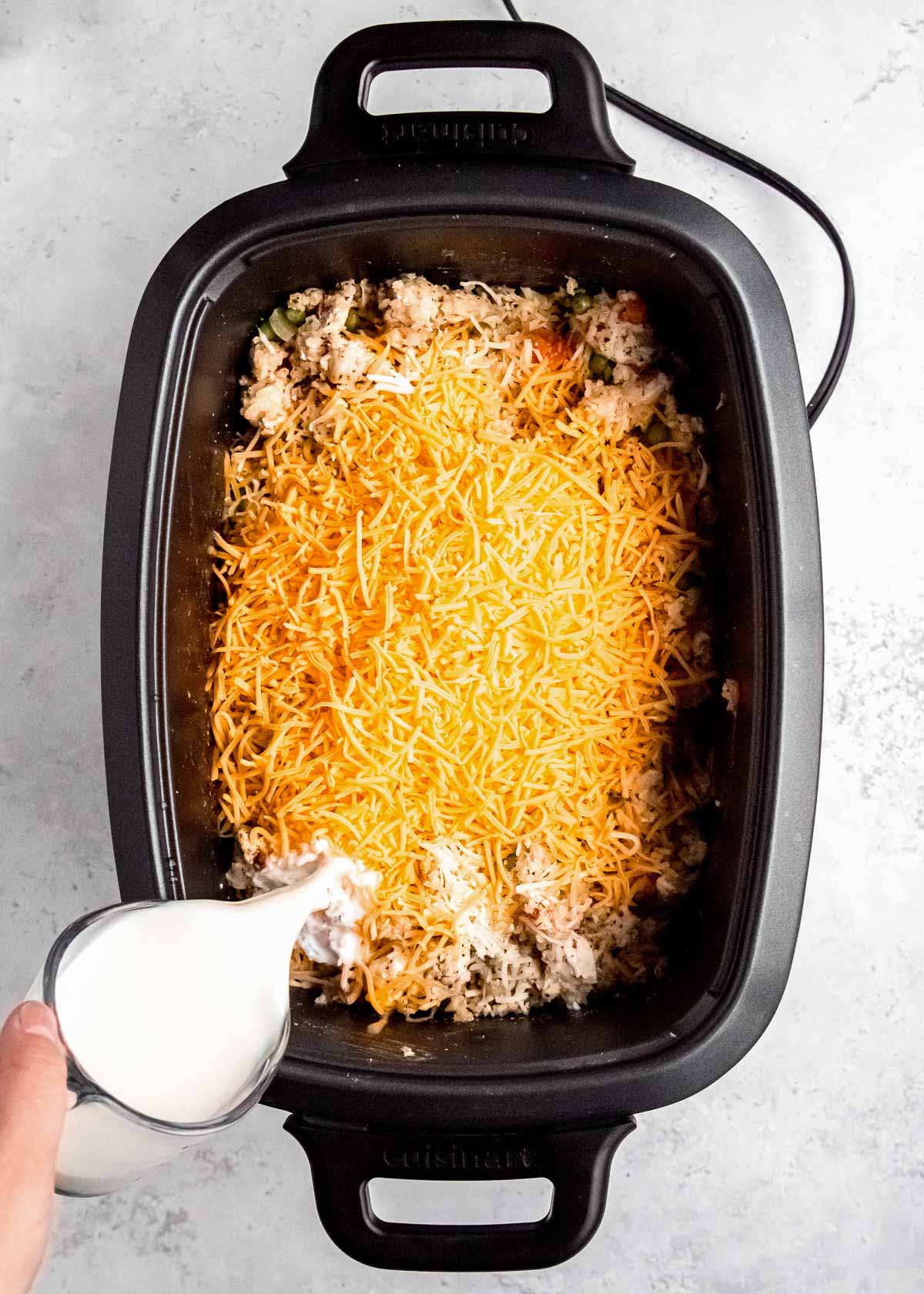 milk being poured into cheesy chicken and rice in a slow cooker