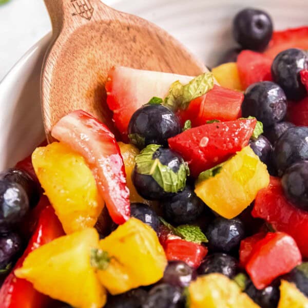 a wooden spoon in a white bowl full of grilled fruit salad