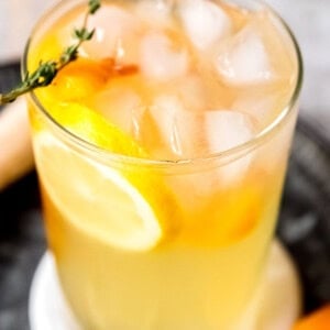 a tall glass of peach bourbon lemonade with thyme and lemon slices
