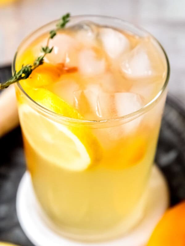 a tall glass of peach bourbon lemonade with thyme and lemon slices