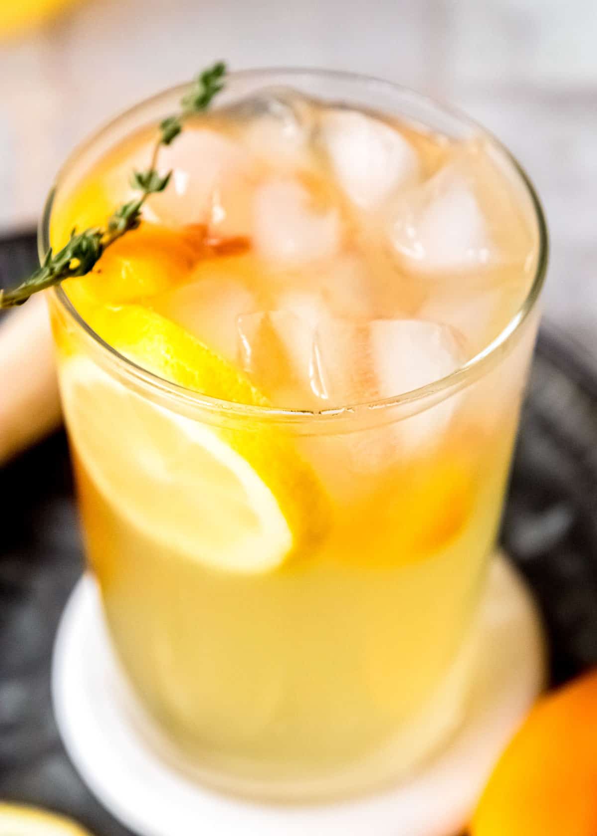 a tall glass of peach bourbon lemonade with thyme and lemon slices