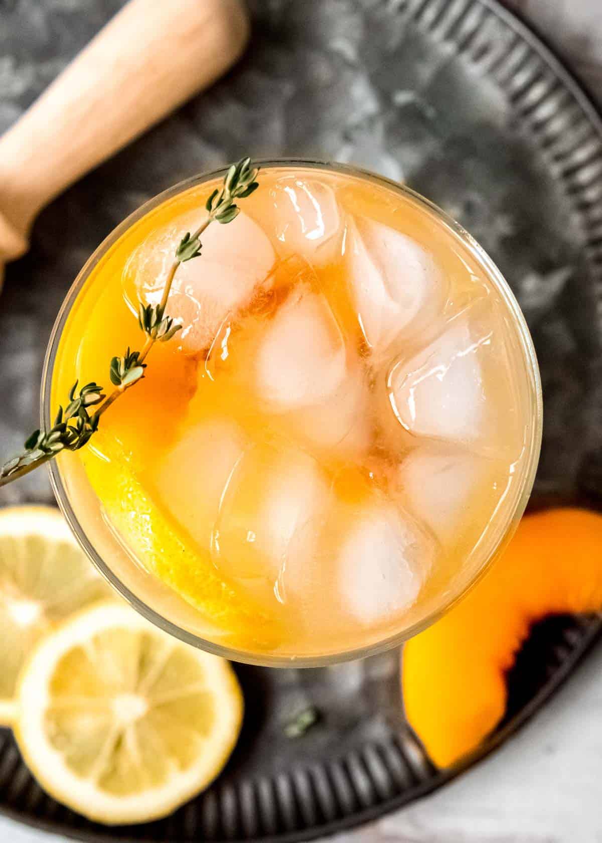 overhead shot showing a glass of boozy lemonade with peaches and thyme