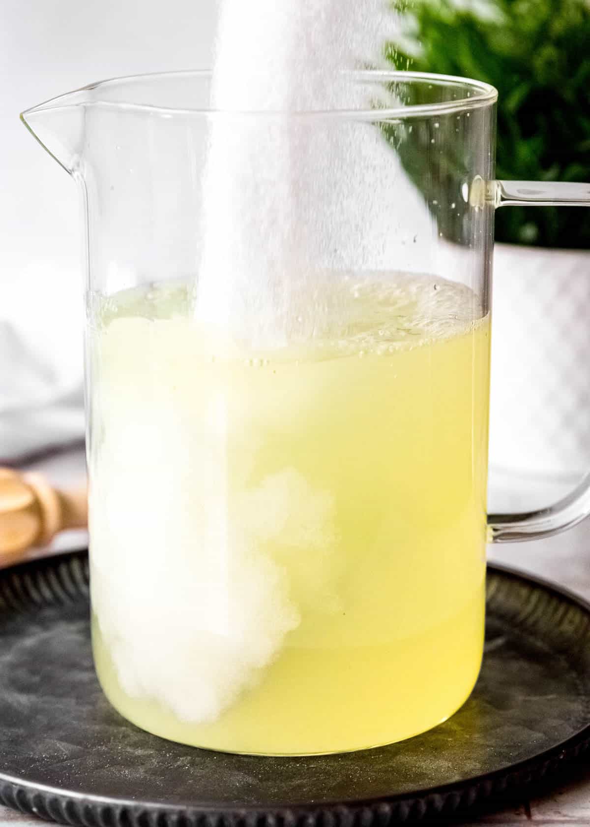 sugar pouring into a pitcher with lemon juice and water