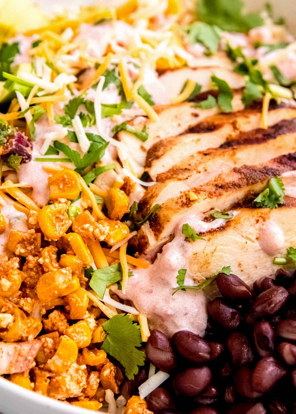 closeup view showing creamy salsa sour cream dressing with chipotle chicken and esquites on a burrito bowl