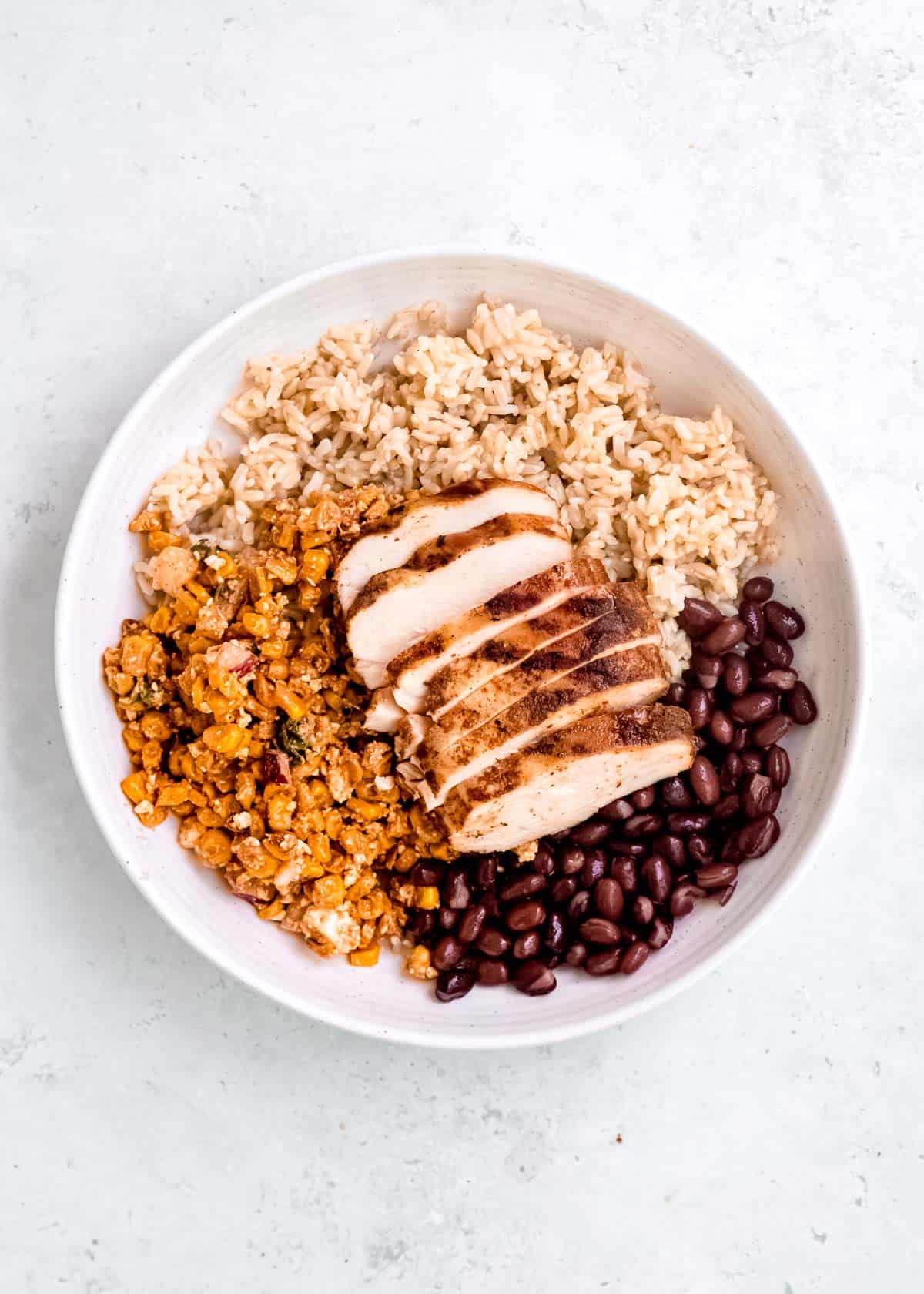 black beans and sliced chipotle chicken in a bowl with brown rice and Mexican street corn salad