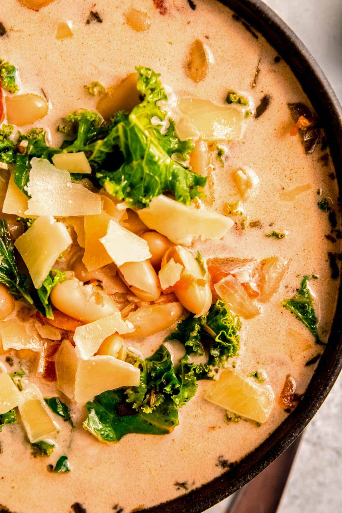 closeup shot of creamy tuscan soup with white beans, kale, and parmesan