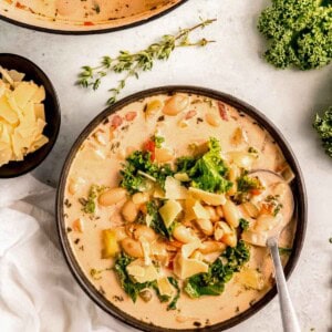 A bowl of creamy Tuscan white bean soup garnished with parmesan; spoon full of a nutritious bite