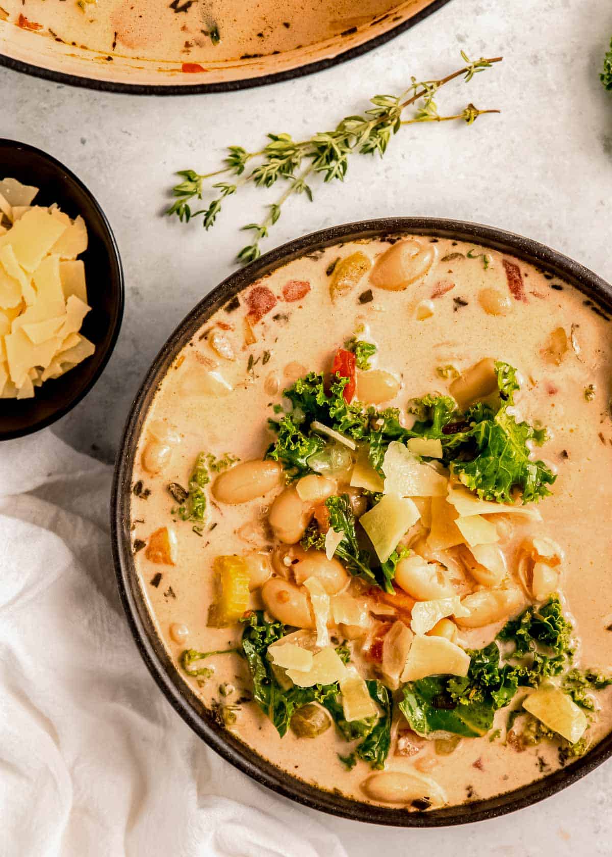 closeup of white bean soup in a black bowl, topped with parmesan cheese garnish