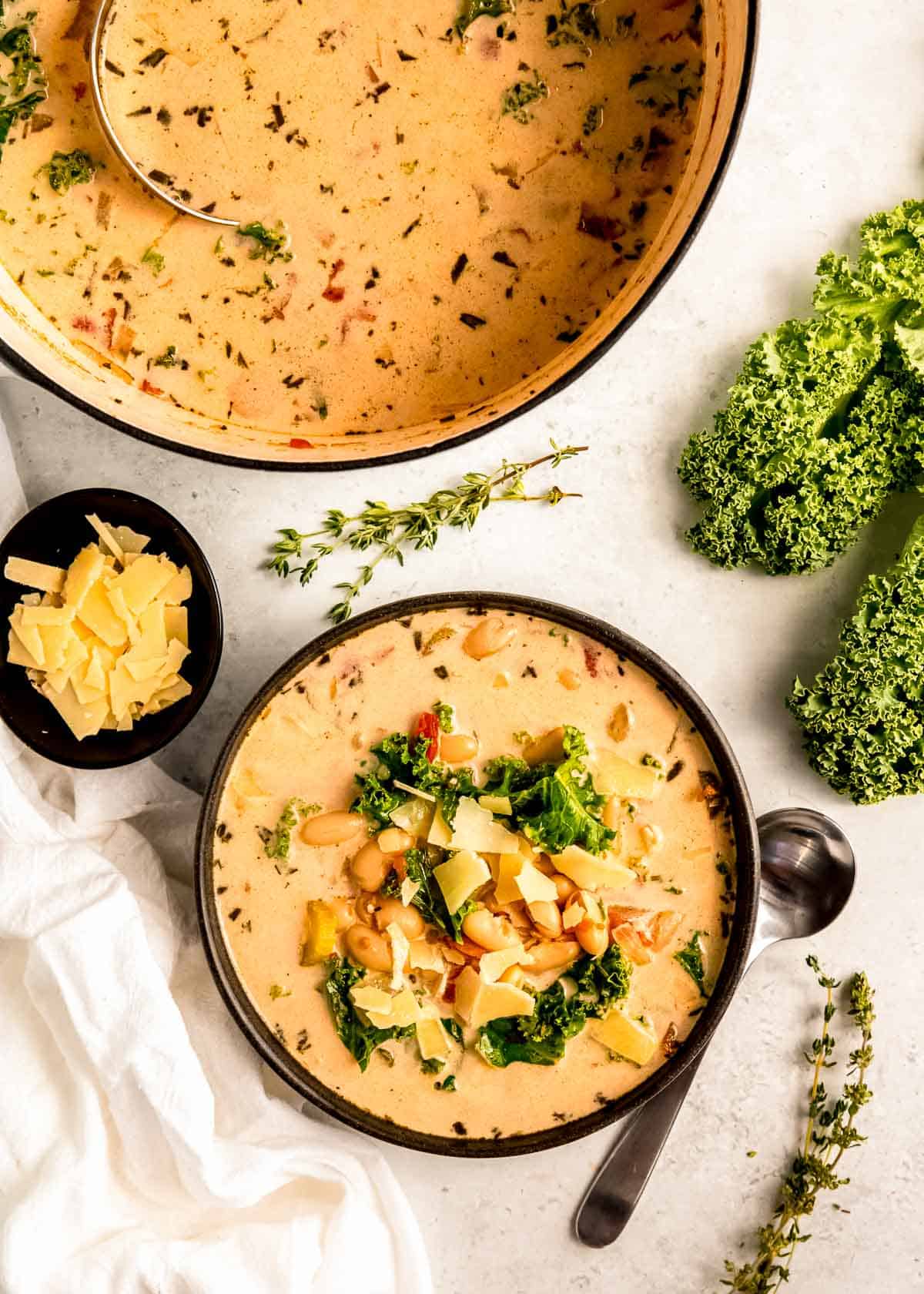 overhead shot showing a full bowl of creamy white bean soup beside a bowl of parmesan and a dutch oven with more soup