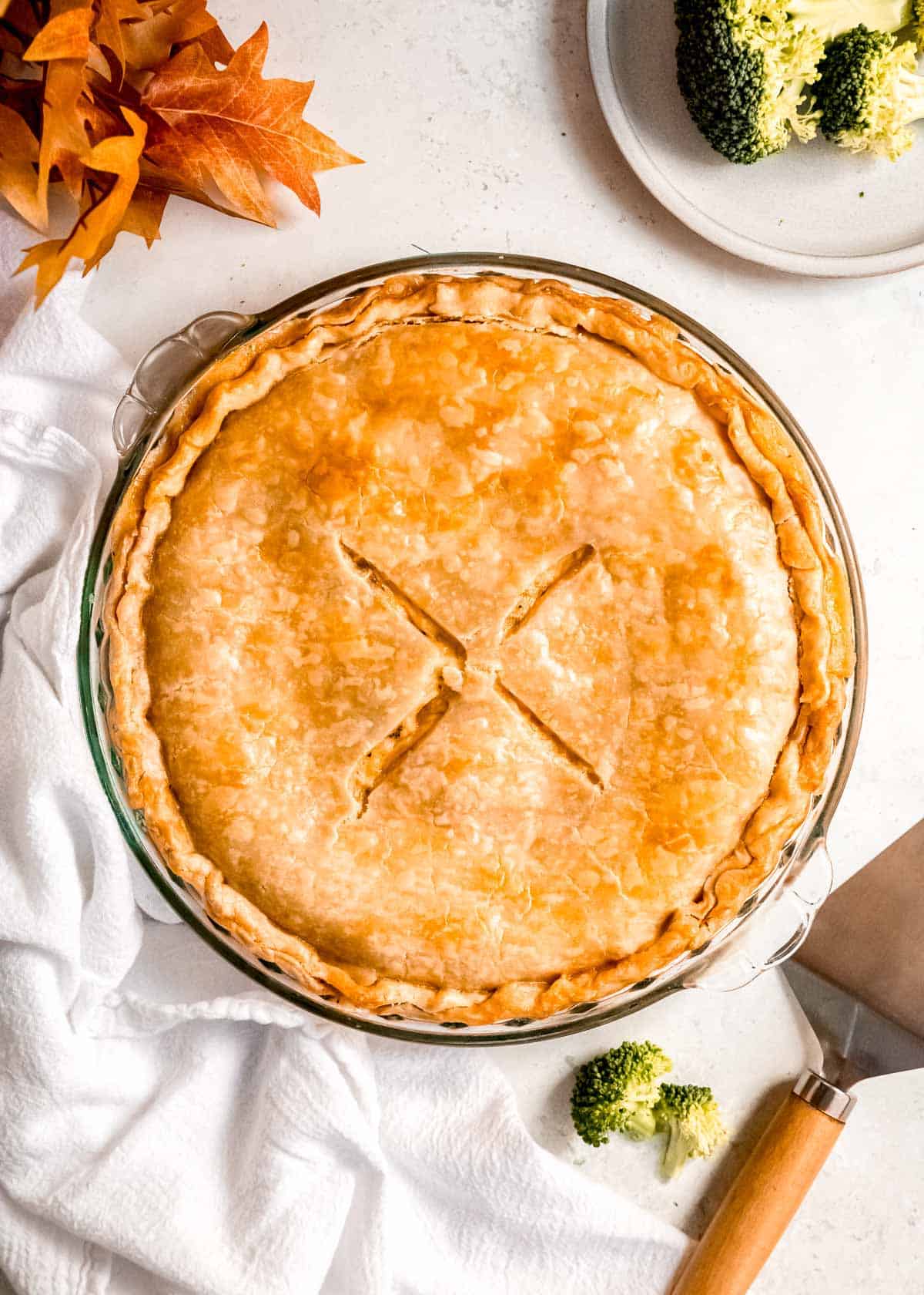 golden brown broccoli cheddar chicken pot pie on a white table with a napkin and broccoli on the side