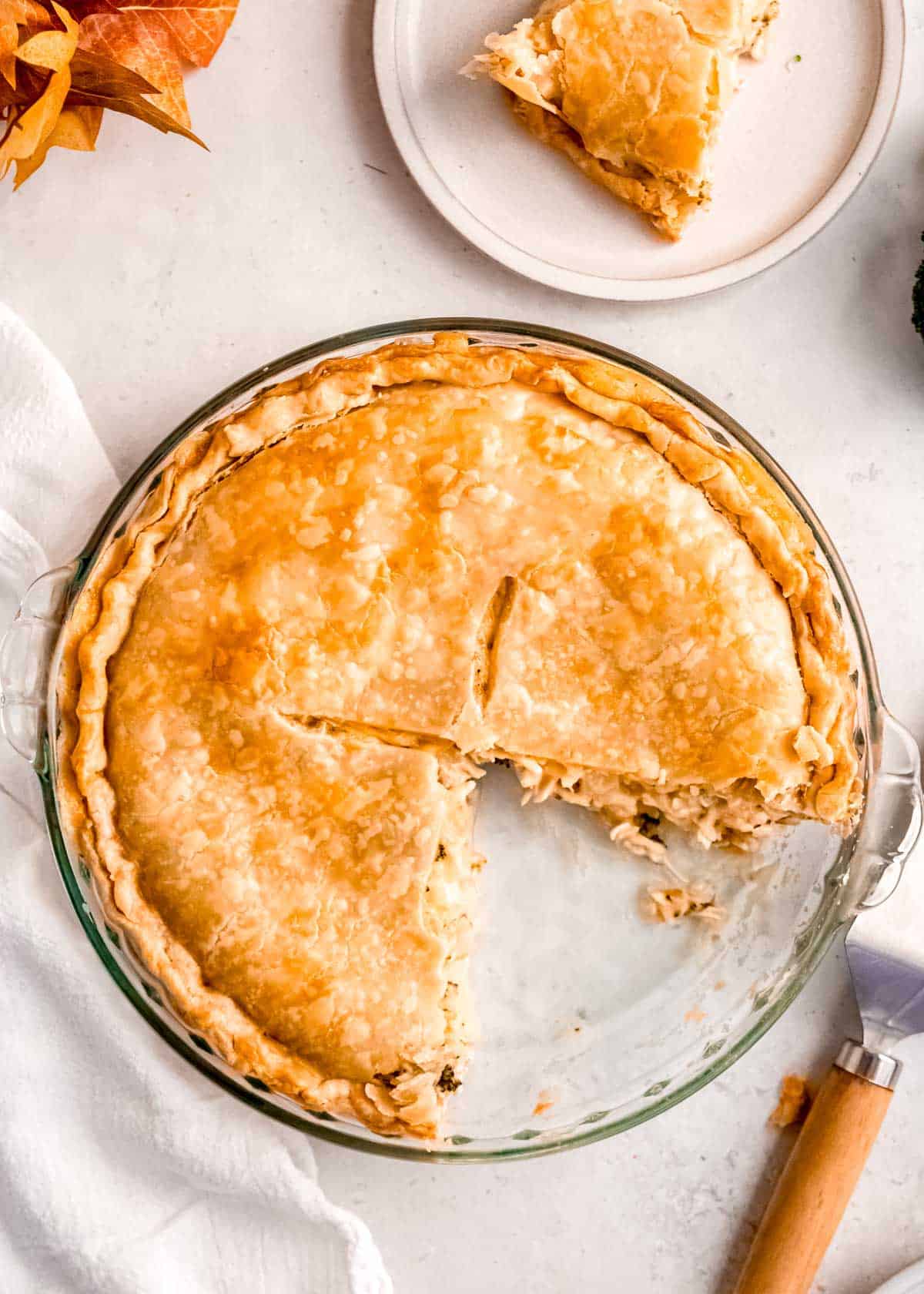 a glass pie pan with a broccoli cheddar chicken pot pie; two slices are missing and on white plates