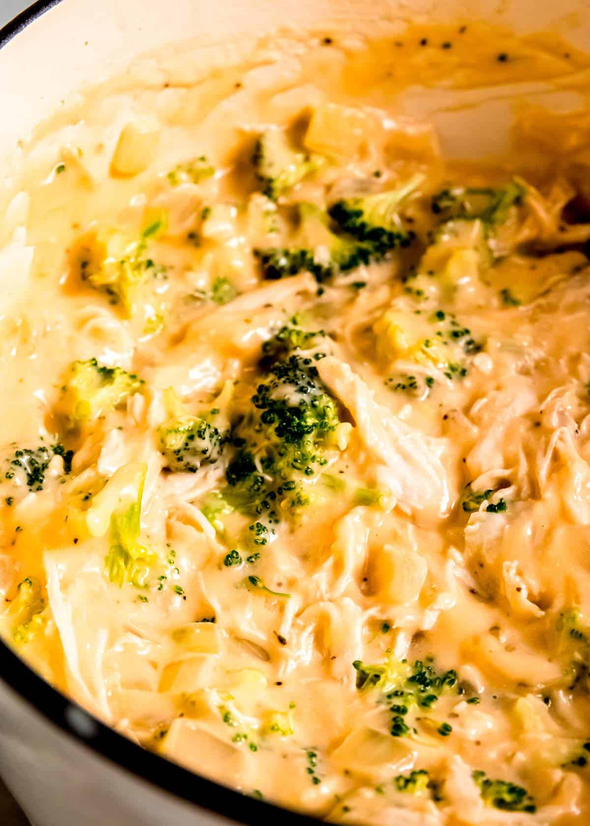 creamy cheesy shredded chicken and broccoli florets in a pot before being poured into a pie crust