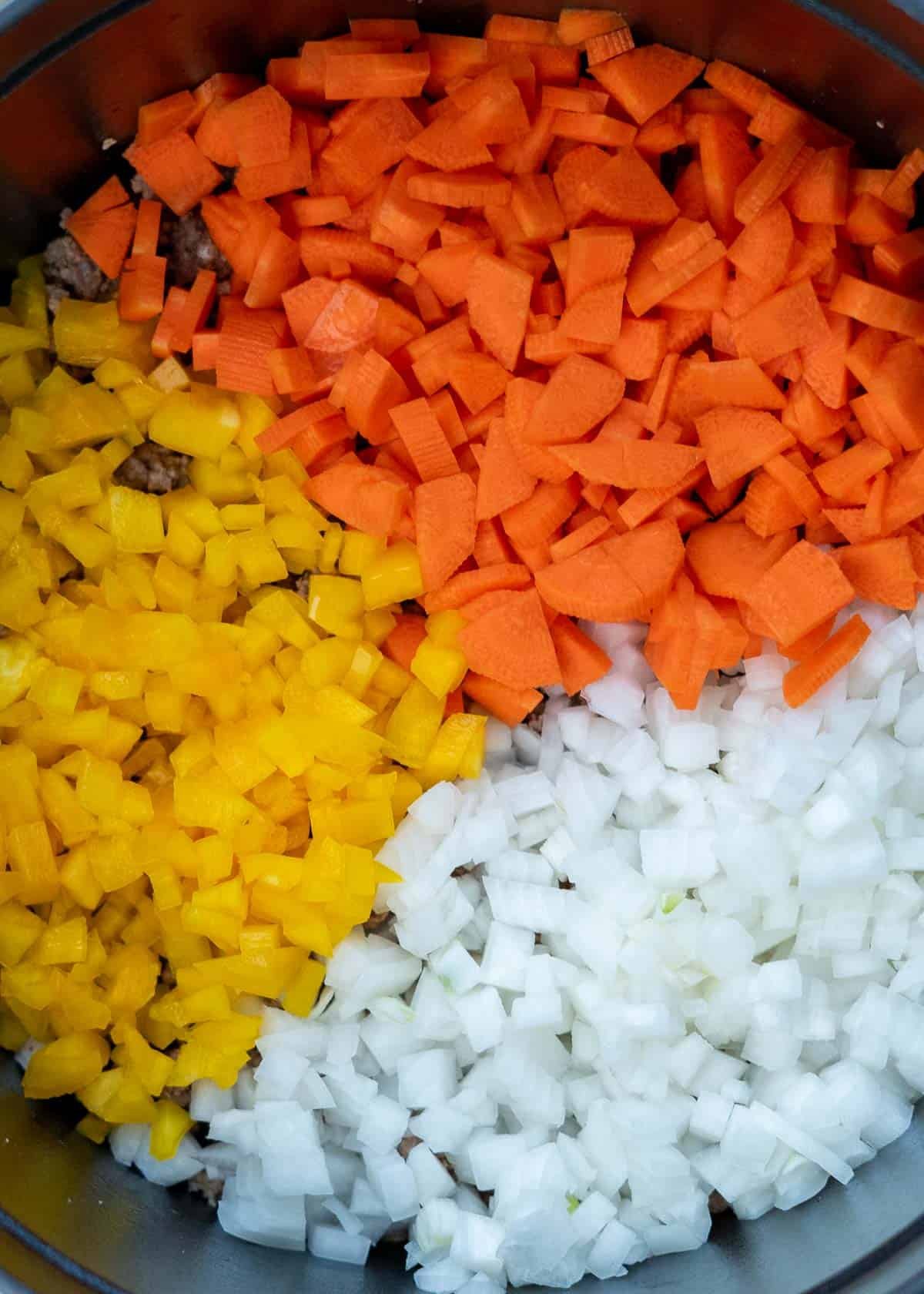 diced yellow pepper, carrots, and onions in a dutch oven with ground beef