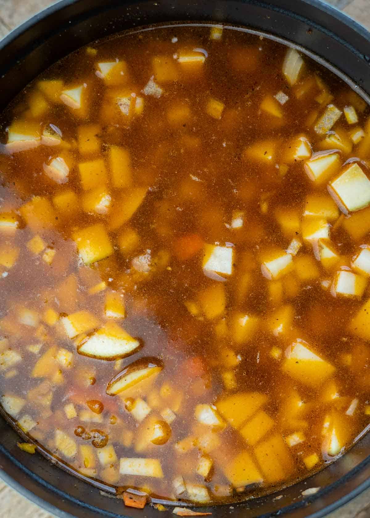 seasonings, broth, worcestershire sauce, and potatoes added to a dutch oven with ground beef and veggies