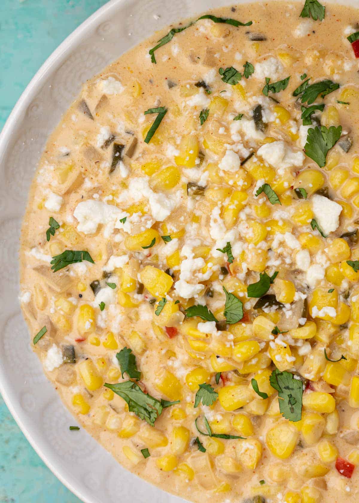 a white bowl filled with creamy, spicy corn soup topped with cilantro and cotija