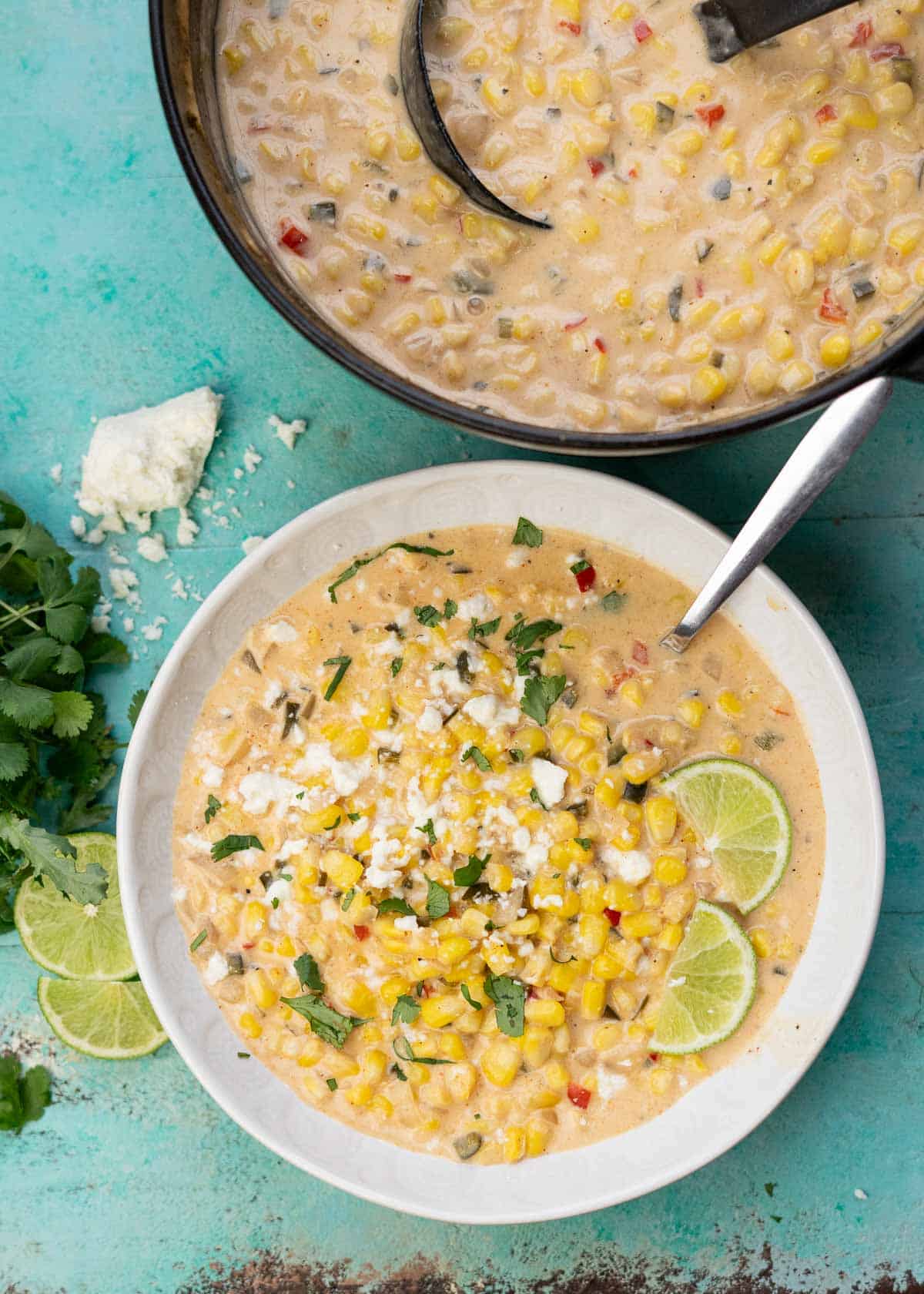 overhead shot showing a bowl of garnished corn soup beside a dutch oven full of the creamy Mexican Street Corn Soup