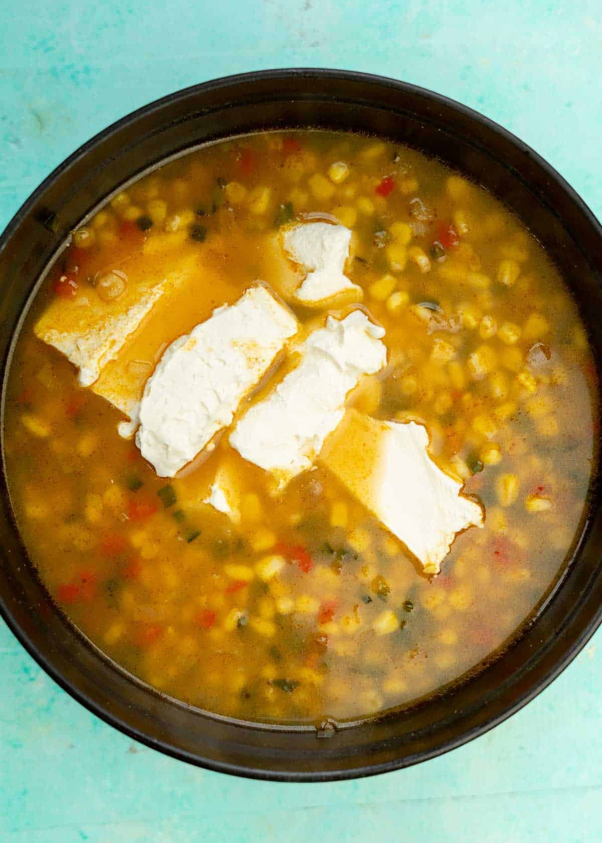 cream cheese added to mexican street corn soup in a dutch oven