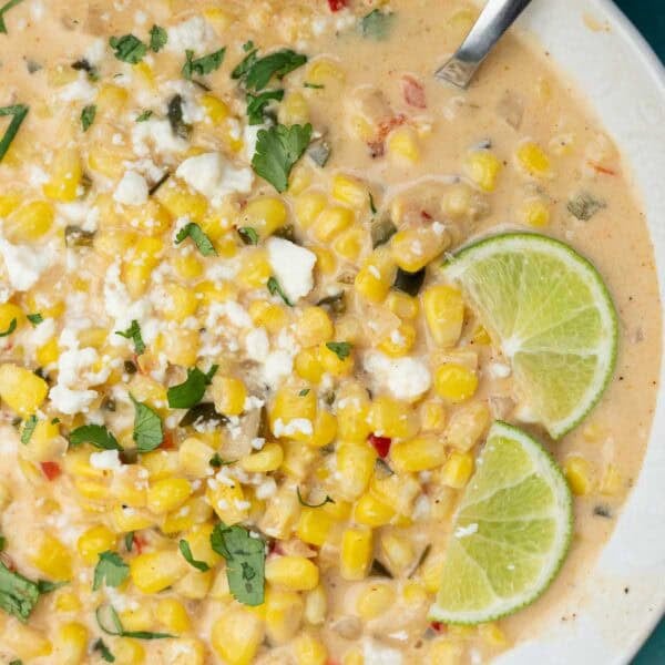 a white bowl filled with Mexican Street Corn Soup, garnished with lime wedges