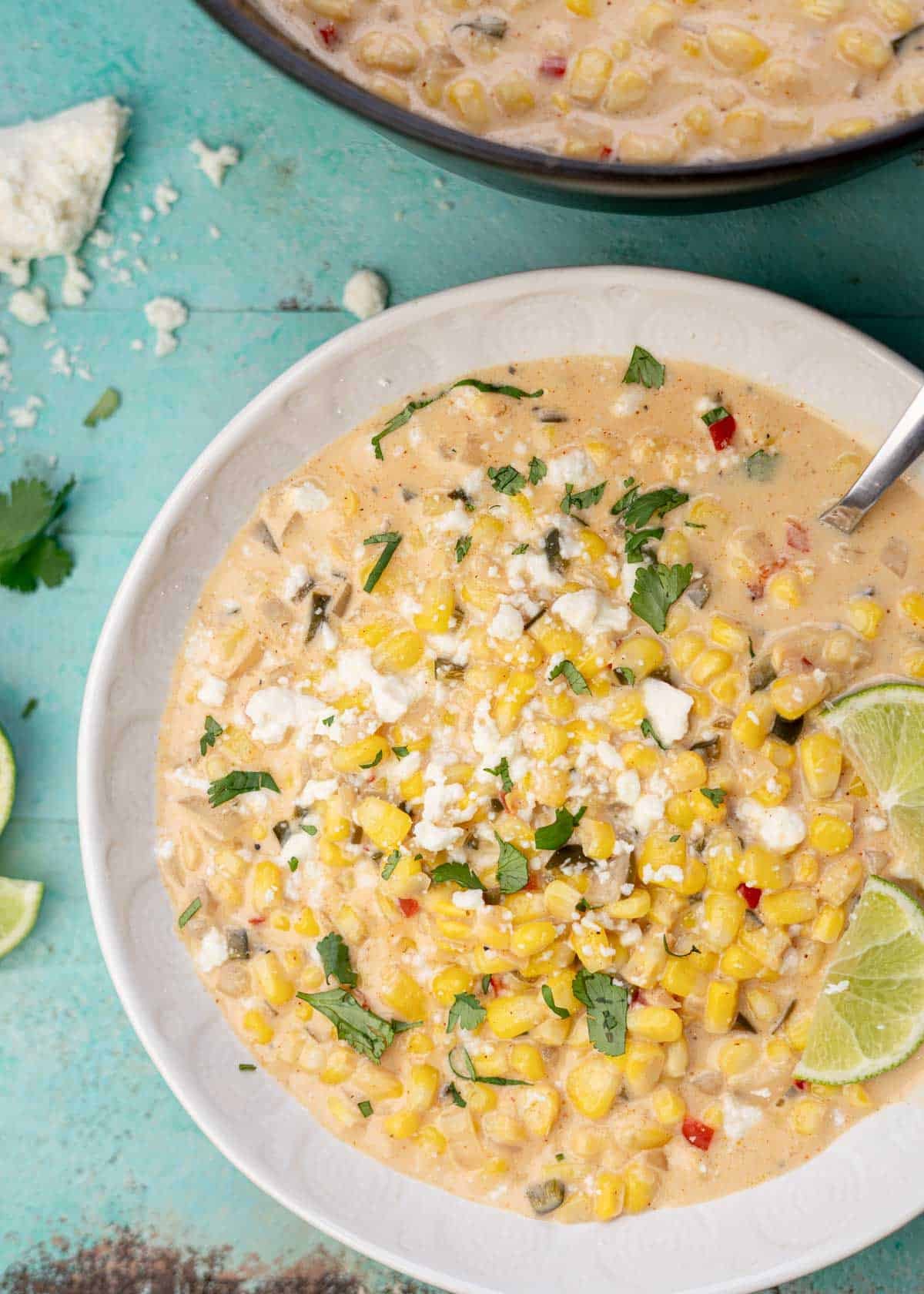 overhead shot showing a bowl of creamy Mexican Street Corn Soup garnished with cilantro, cotija cheese, and lime wedges