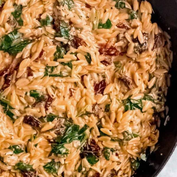 creamy tuscan orzo in a skillet with spinach, thyme, parmesan, and sundried tomatoes