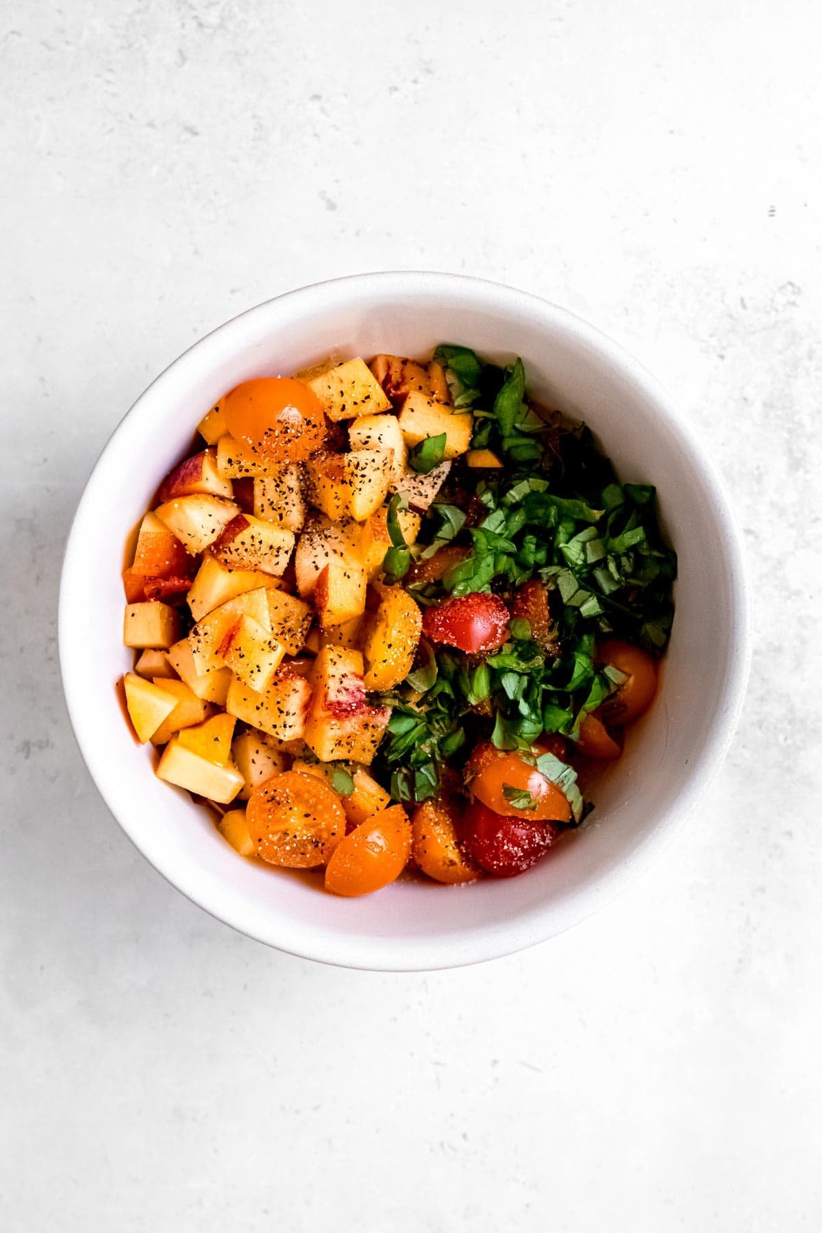 chopped tomatoes, peaches, and basil in a white bowl