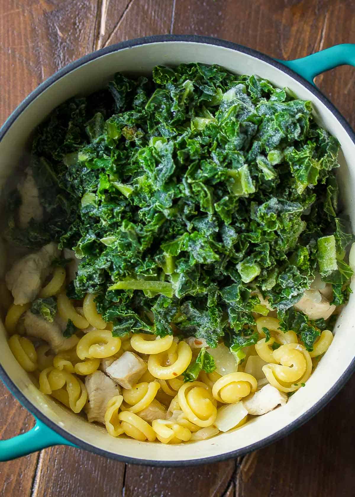 kale and lemon juice added into a pot with cooked pasta and onion