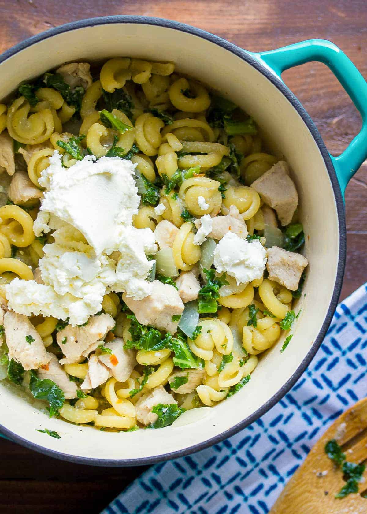 crumbled goat cheese added into a pot with kale and pasta