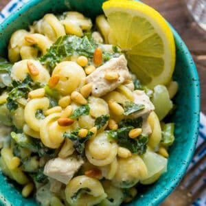 overhead shot showing creamy goat cheese pasta in a bowl topped with pine nuts and a lemon wedge