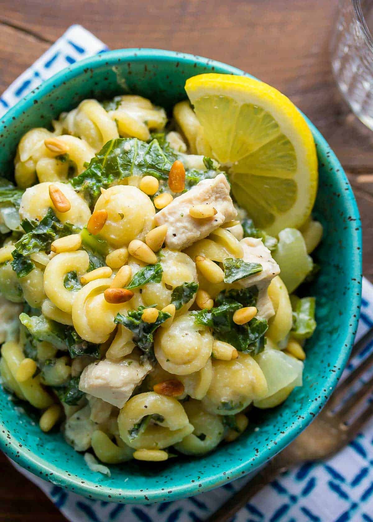 overhead shot showing creamy goat cheese pasta in a bowl topped with pine nuts and a lemon wedge