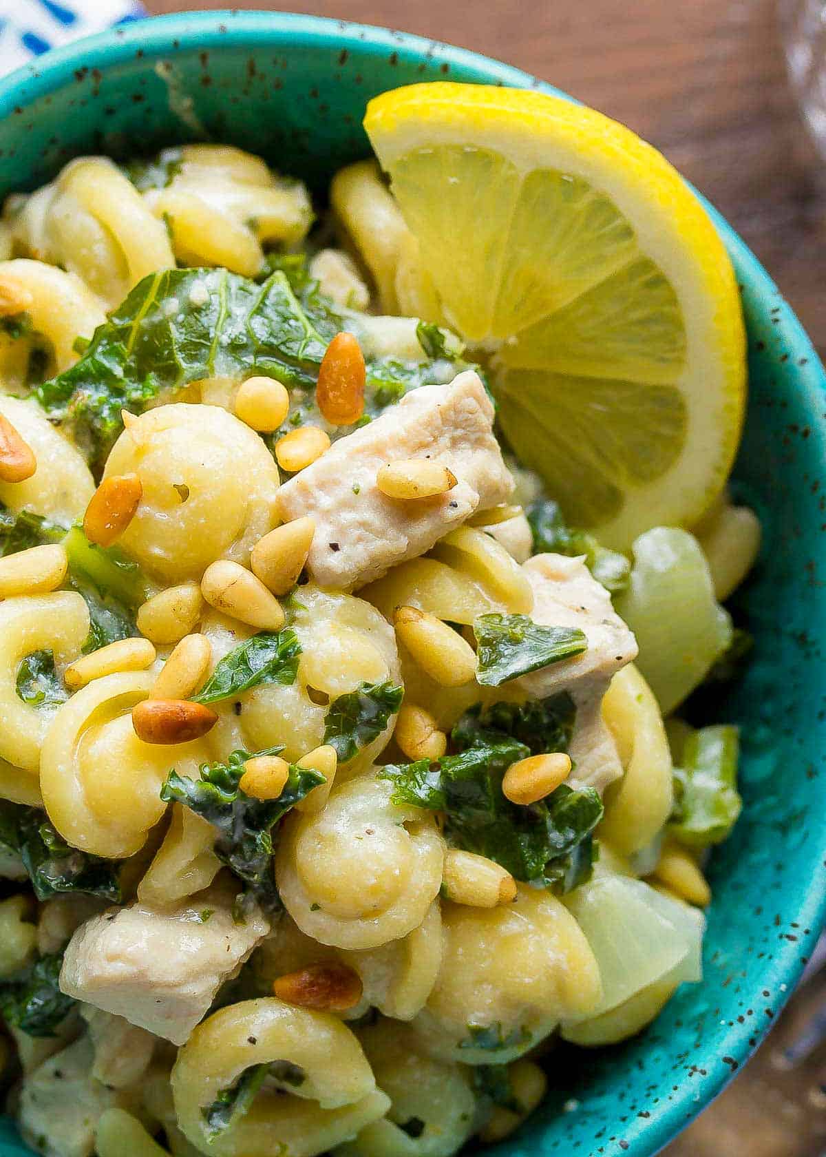 closeup showing super creamy goat cheese pasta with kale, pine nuts, and a lime wedge on the side