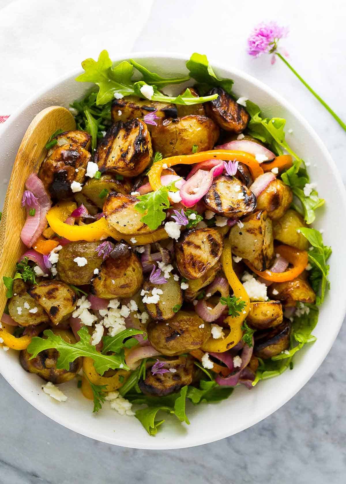 overhead shot showing fresh herbs and feta cheese over grilled potato salad over arugula mixed with lemon parsley vinaigrette