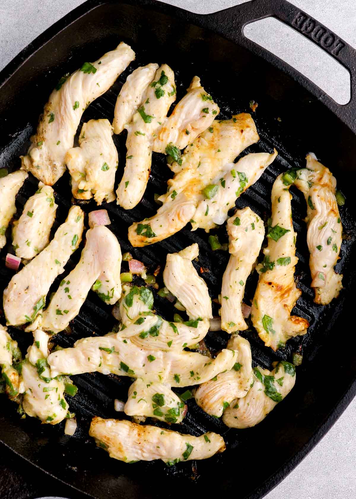 strips of marinated chicken breast cooking in a cast iron grill pan