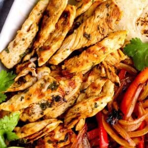 strips of juicy fajita chicken on a platter with marinated vegetables and tortillas