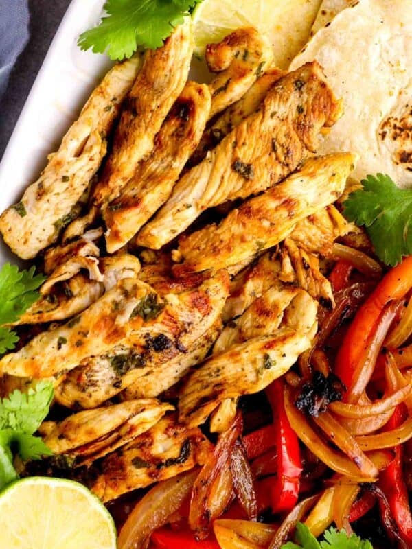 strips of juicy fajita chicken on a platter with marinated vegetables and tortillas