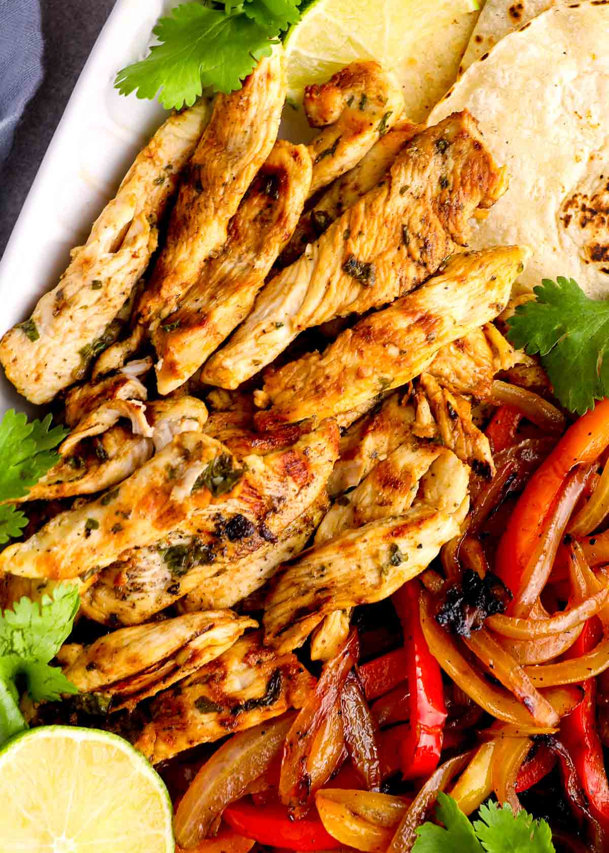 strips of juicy fajita chicken on a platter with marinated vegetables and tortillas