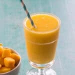 a wine slushie in a glass with a straw beside a bowl of frozen mango