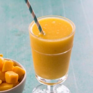 a wine slushie in a glass with a straw beside a bowl of frozen mango