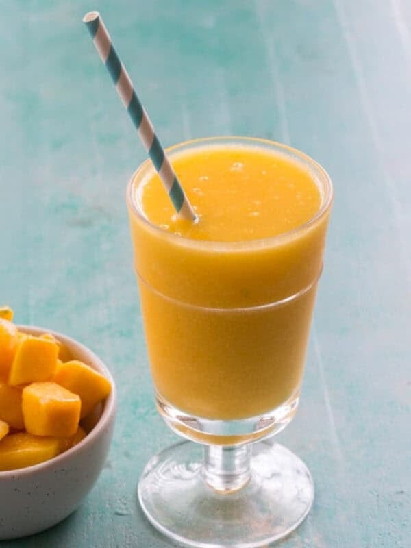 a wine slushie in a glass with a straw beside a bowl of frozen mango