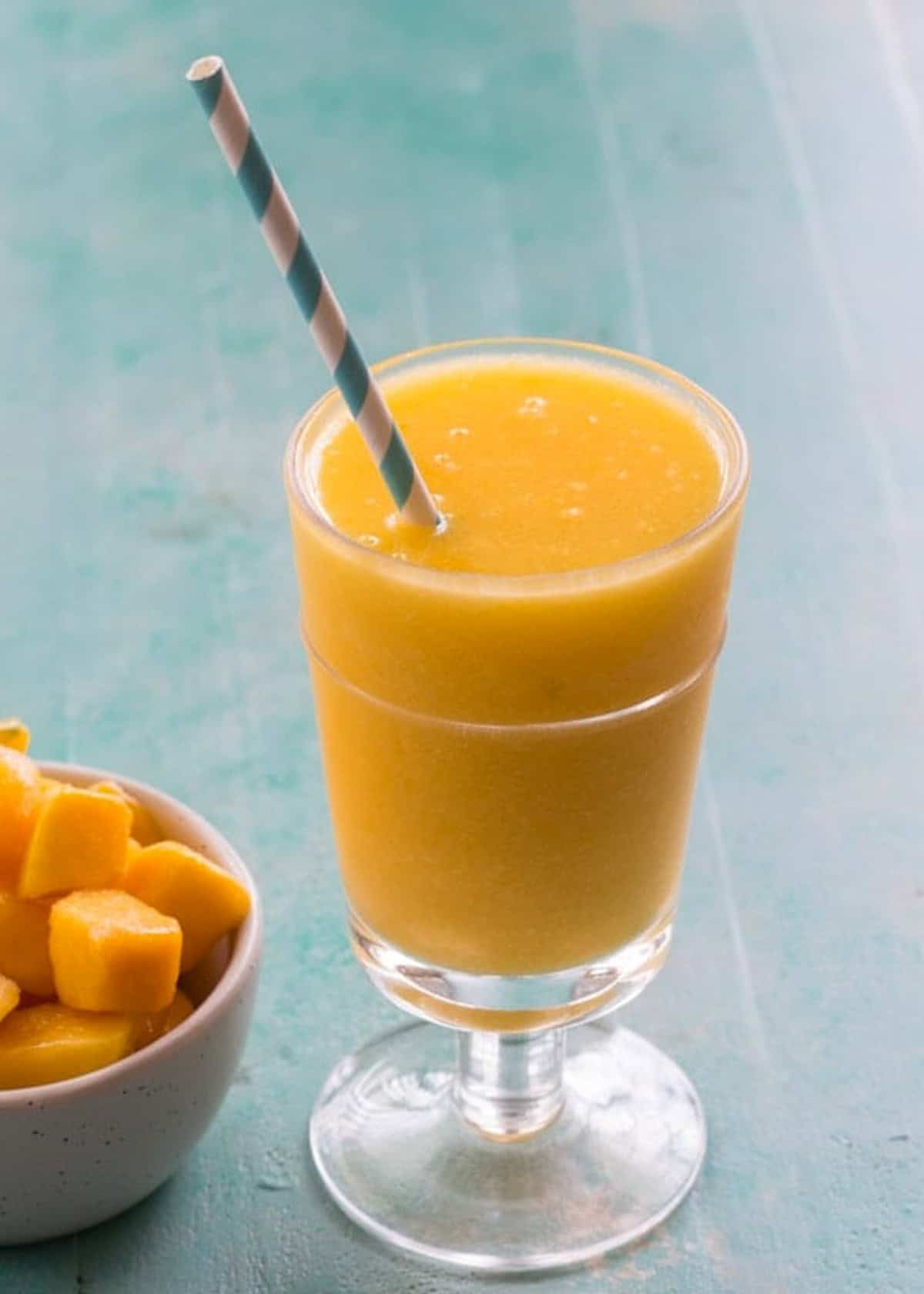 a wine slushie in a glass with a straw beside a bowl of frozen mango