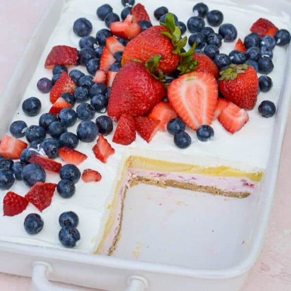 a baking dish filled with layered strawberry cheesecake bars topped with fresh fruit