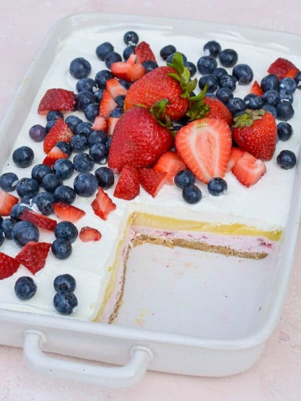 a baking dish filled with layered strawberry cheesecake bars topped with fresh fruit
