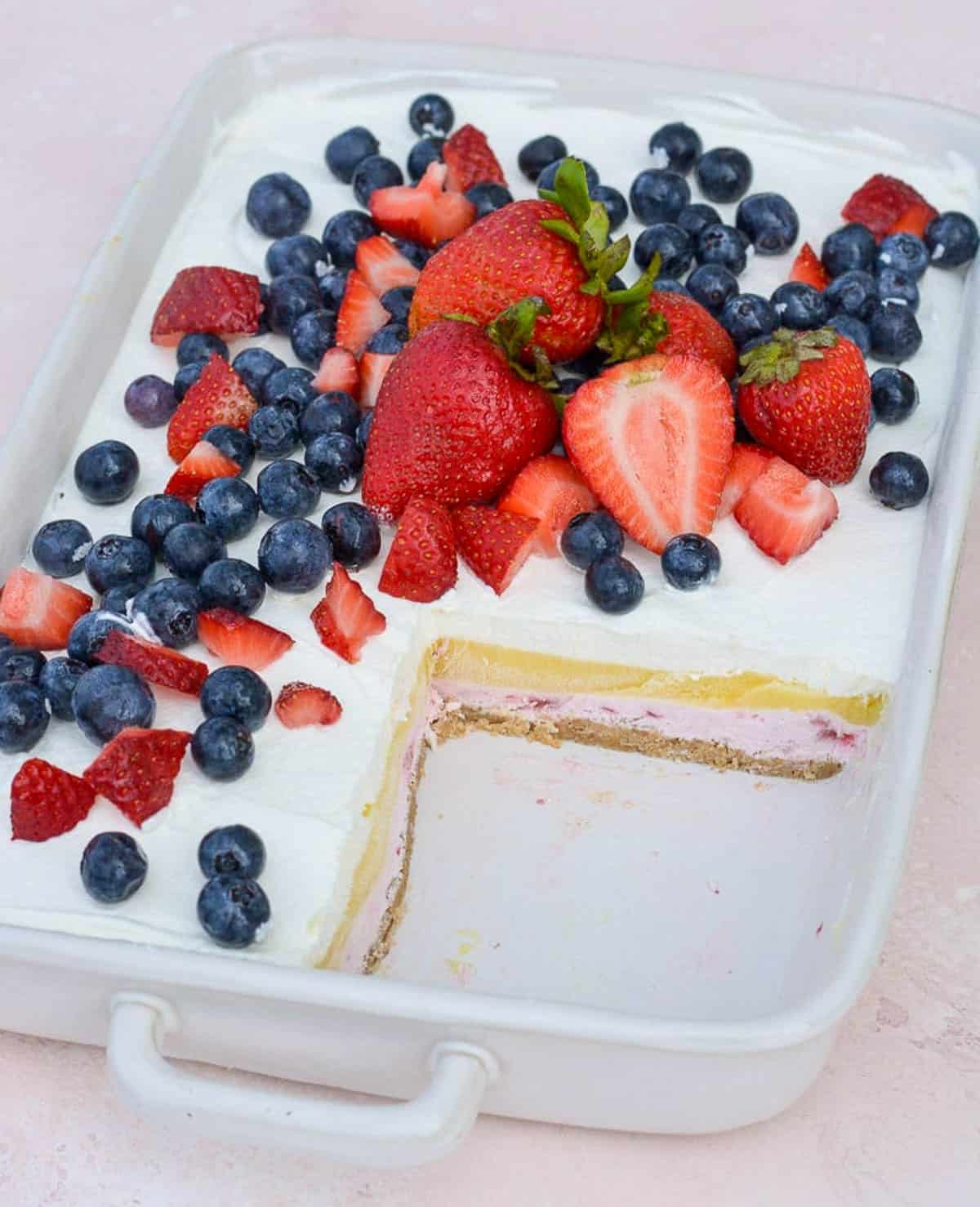 a baking dish filled with layered strawberry cheesecake bars topped with fresh fruit