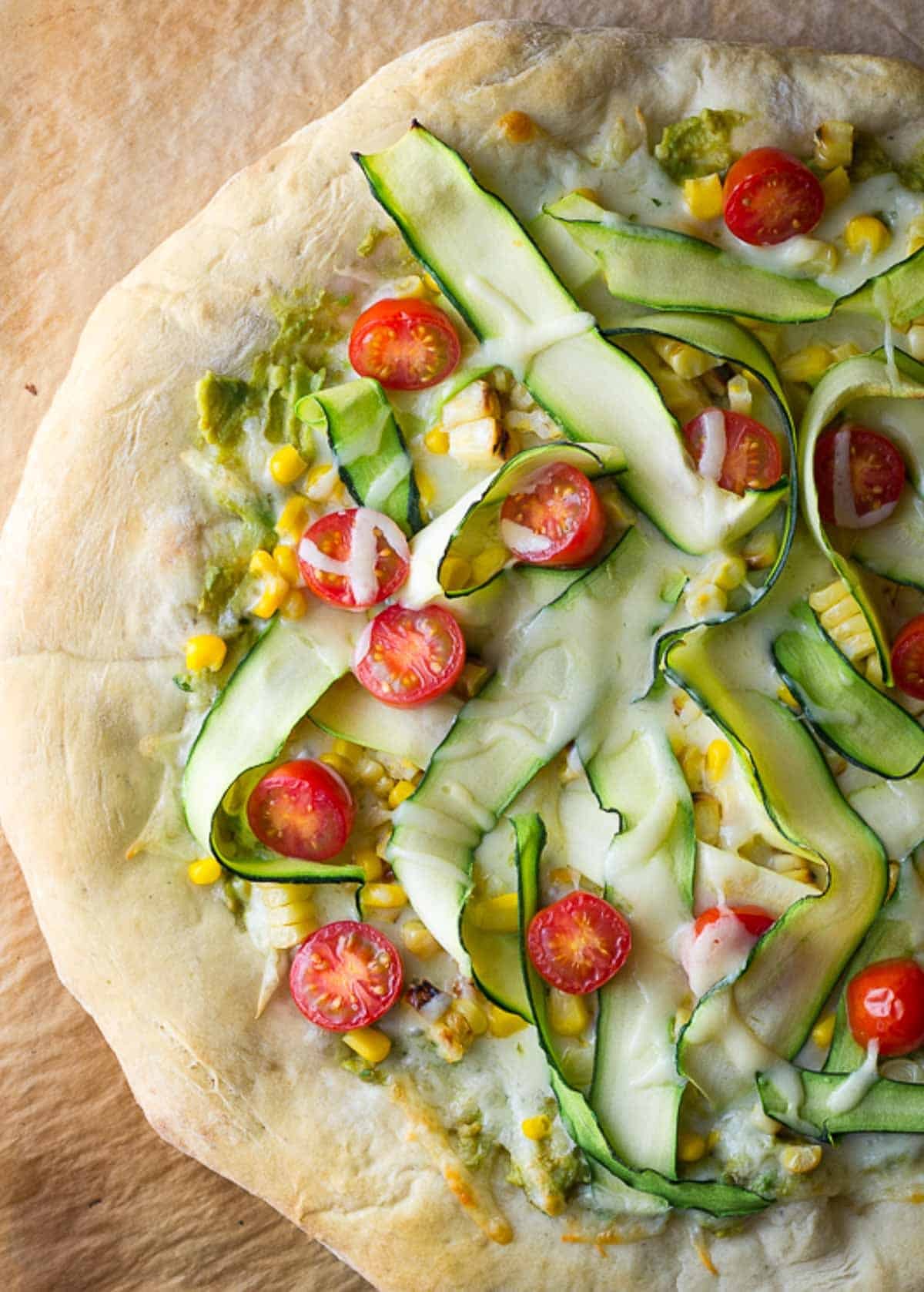 overhead view showing flatbread pizza recipe with mozzarella, zucchini, tomatoes, and corn