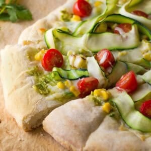 a flatbread pizza topped with avocado, corn, zucchini, tomatoes, and mozzarella cheese