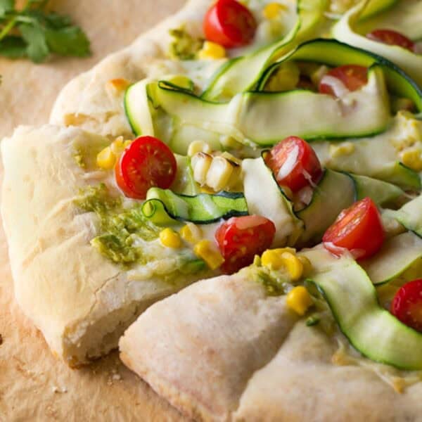 a flatbread pizza topped with avocado, corn, zucchini, tomatoes, and mozzarella cheese