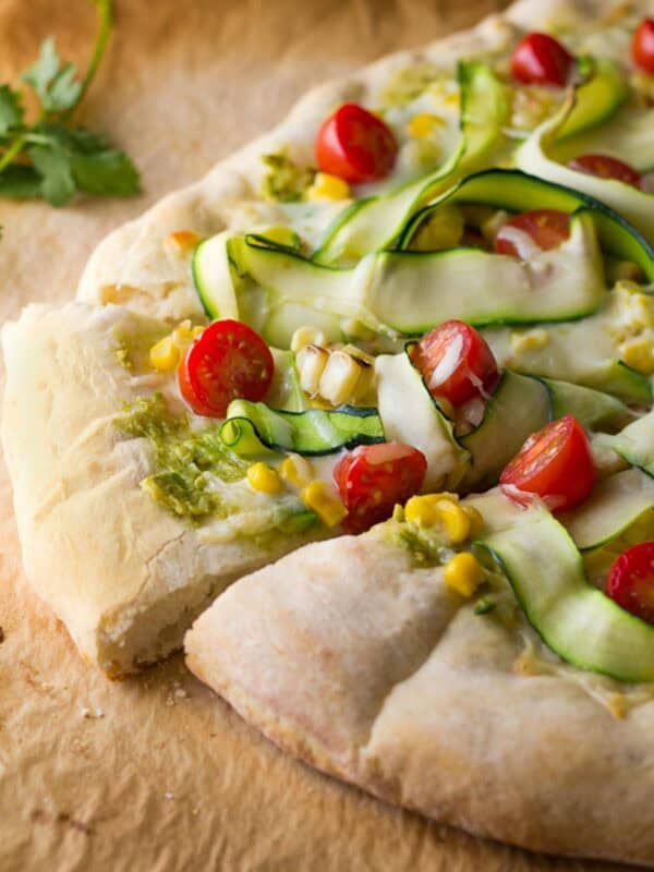 a flatbread pizza topped with avocado, corn, zucchini, tomatoes, and mozzarella cheese